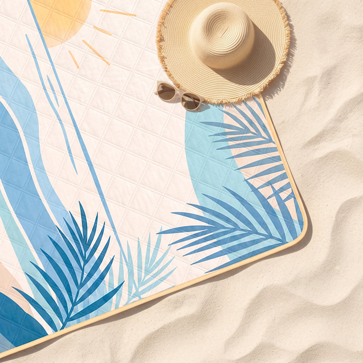 Close-up of the Ocean Sunshine State quilted beach blanket on sand with a sun hat and sunglasses